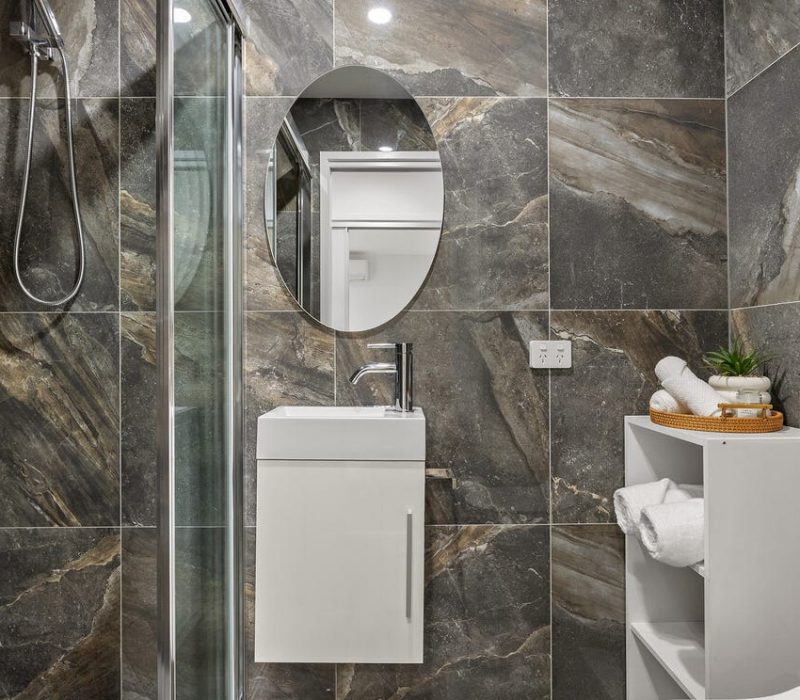 Ensuite with shower, round mirror and stone-look tiles