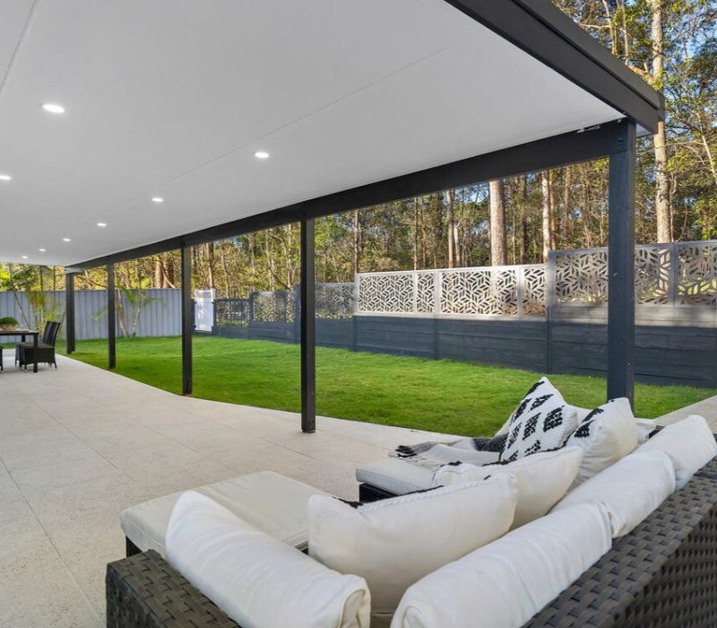 Covered outdoor patio with seating area and expansive lawn