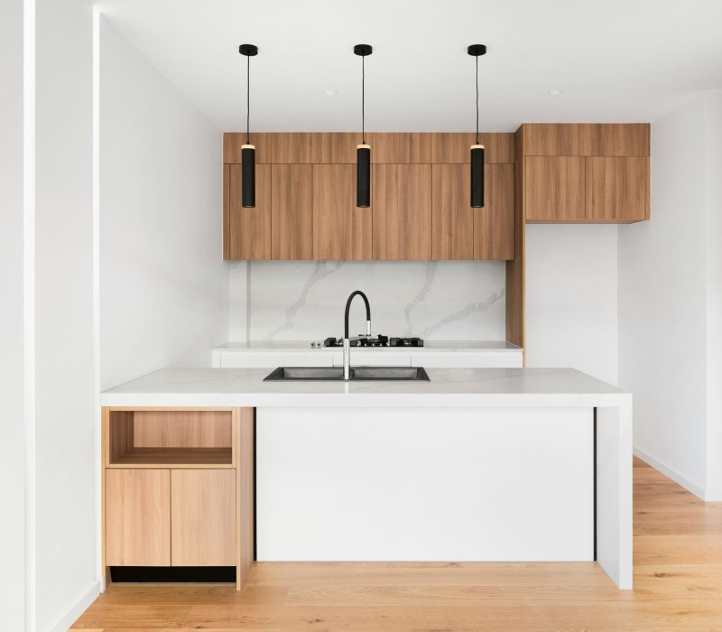 Contemporary kitchen with wood cabinetry, white island and black pendant lights